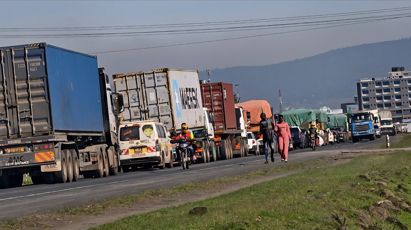 A long line of heavy trucks and passenger vehicles stuck in traffic on the Nairobi-Nakuru highway under a clear sky.