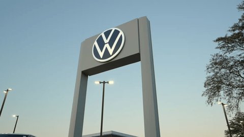 The large blue and white circular logo of Volkswagen seen on file 276076.png mounted on a modern commercial building facade against a clear blue sky.