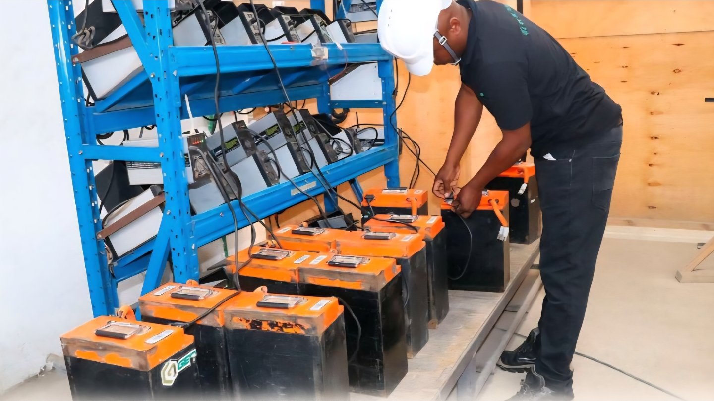 Technician maintaining electric motorcycle batteries arranged on charging racks inside a battery swapping station.