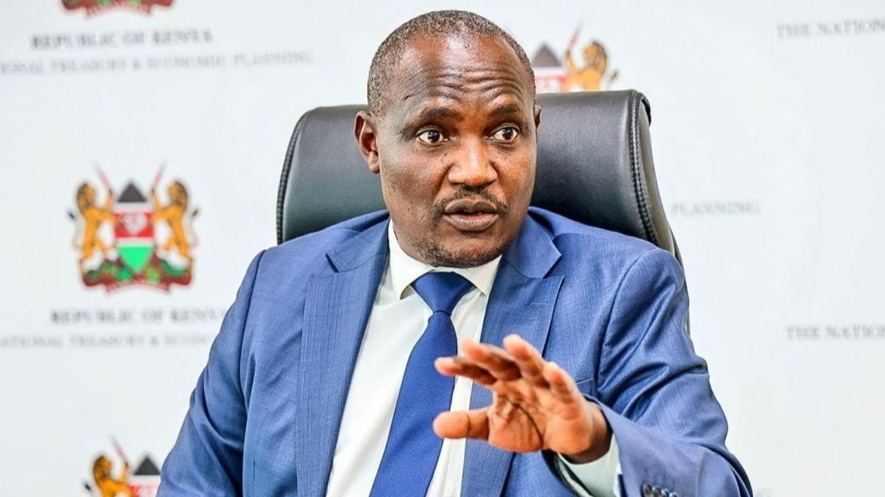 A close-up professional photograph of Treasury Cabinet Secretary John Mbadi speaking at a podium during a government press briefing in Nairobi.