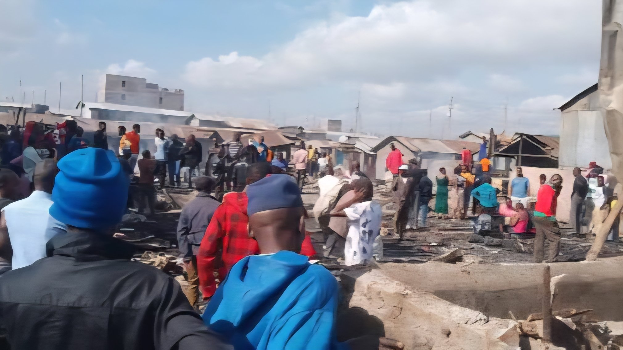 A group of residents and onlookers stand near a demolition site in Mukuru Kwa Njenga as dust rises from flattened structures.