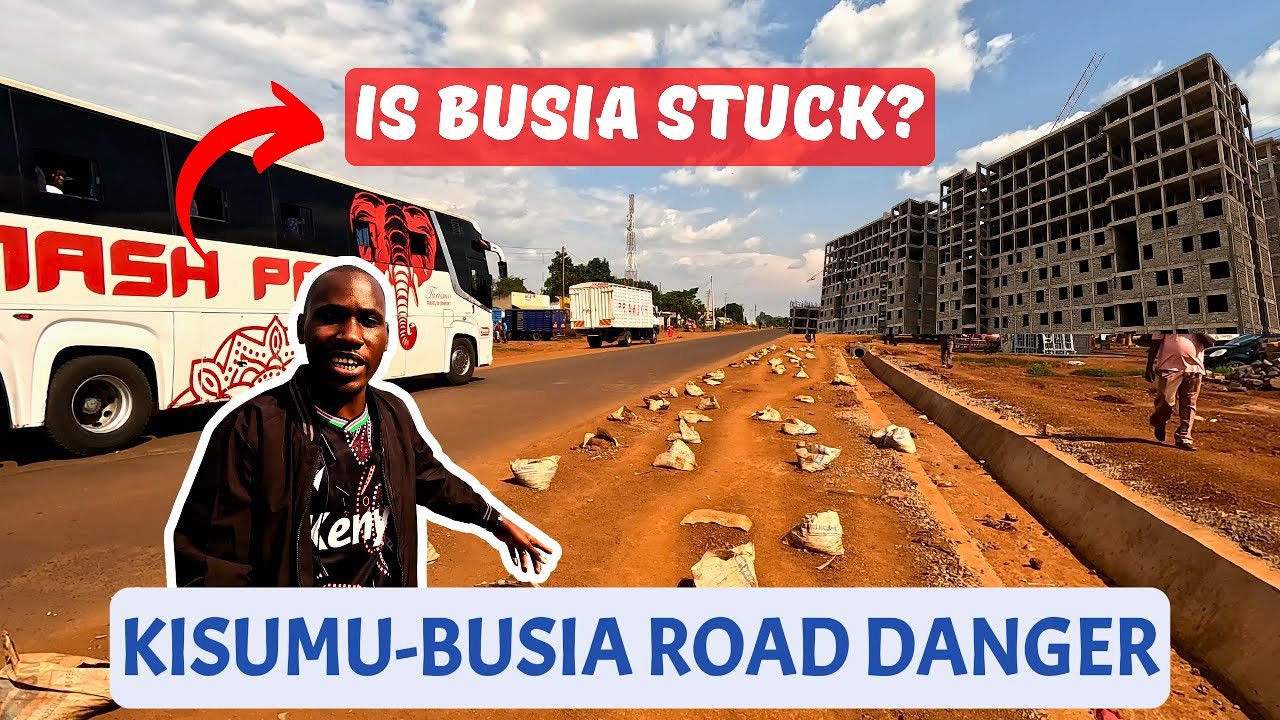A large green commercial truck driving on the Busia-Kisumu highway past a significant erosion gully and deep potholes on the dirt shoulder and road edge.