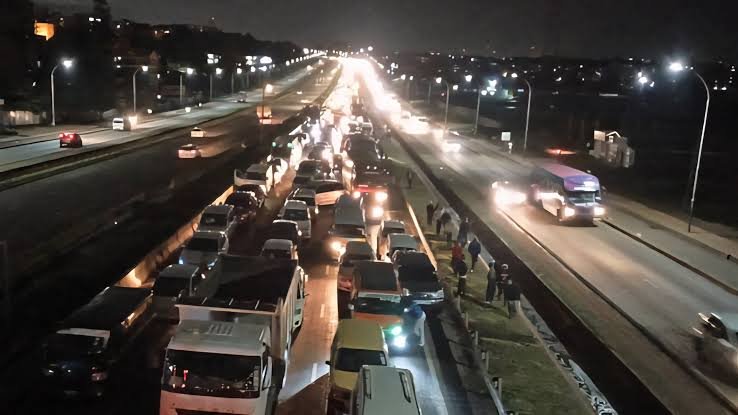A dense line of white and yellow matatus and private cars in a heavy traffic jam on a multi-lane highway in Nairobi, Kenya.
