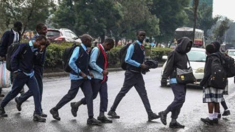 Kenyan students wearing school uniforms walking together on a school compound.