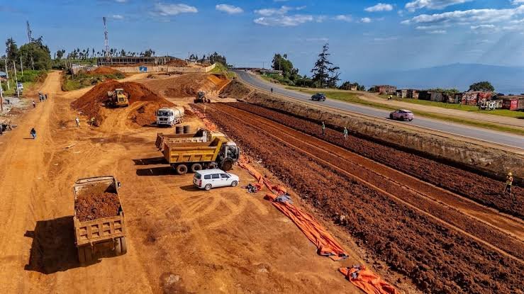 Earthmoving machinery and heavy road construction equipment operating along a active rural highway construction site in Kenya.