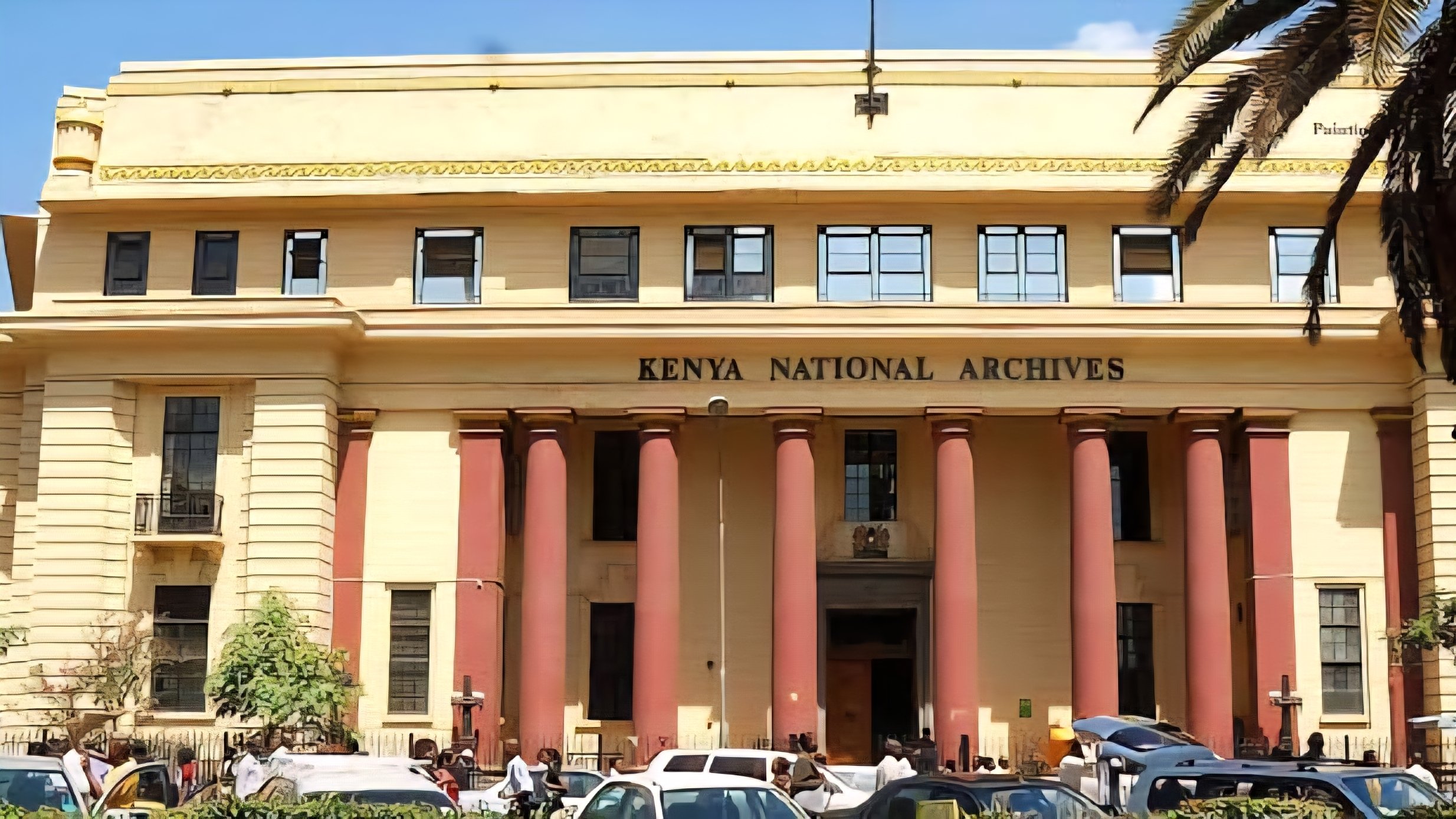 Exterior view of the Kenya National Archives building on a busy street in Nairobi, showing its classical architectural features.