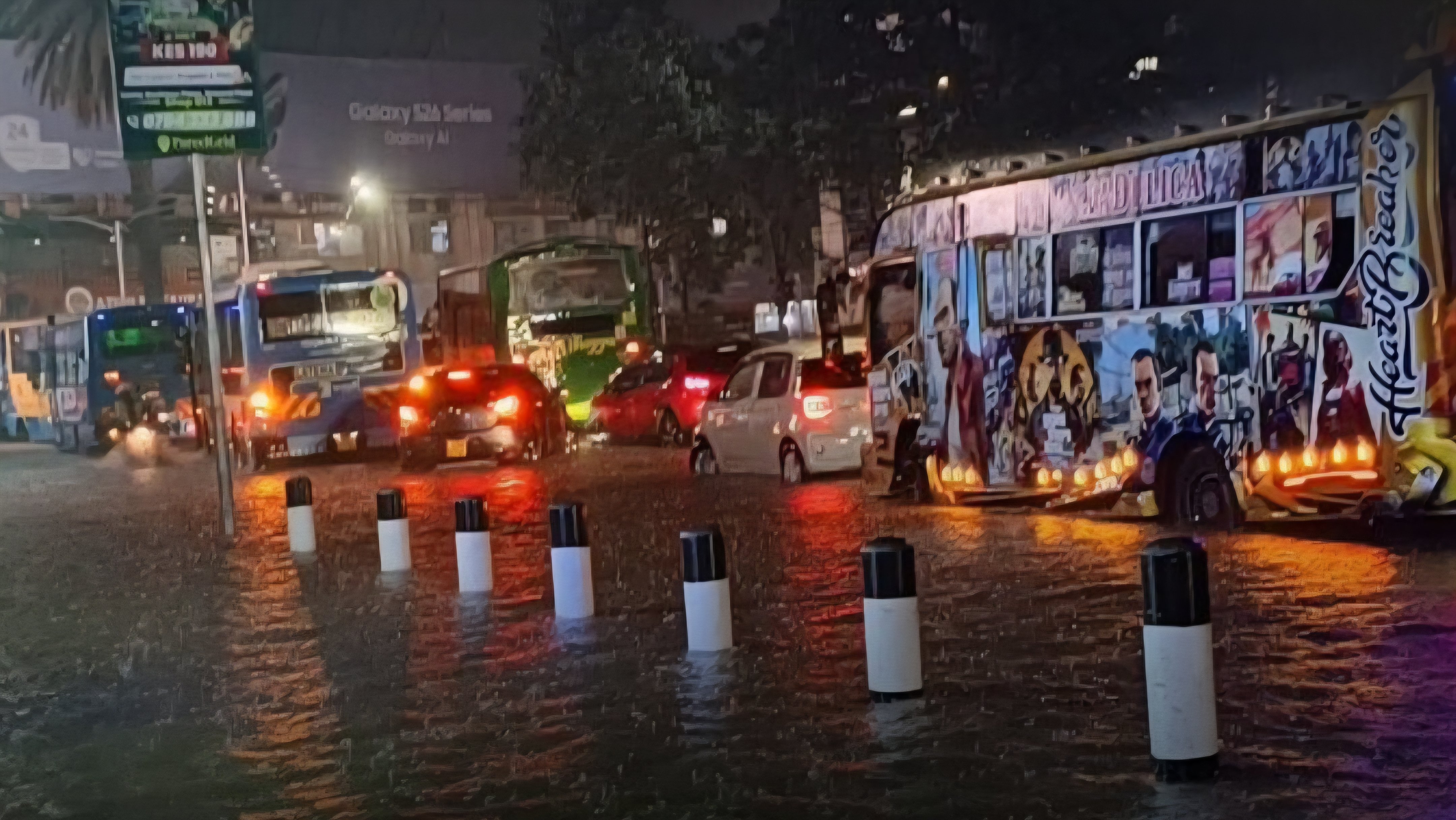 A flooded Nairobi street at night with a bus and cars navigating deep water near black and white bollards.