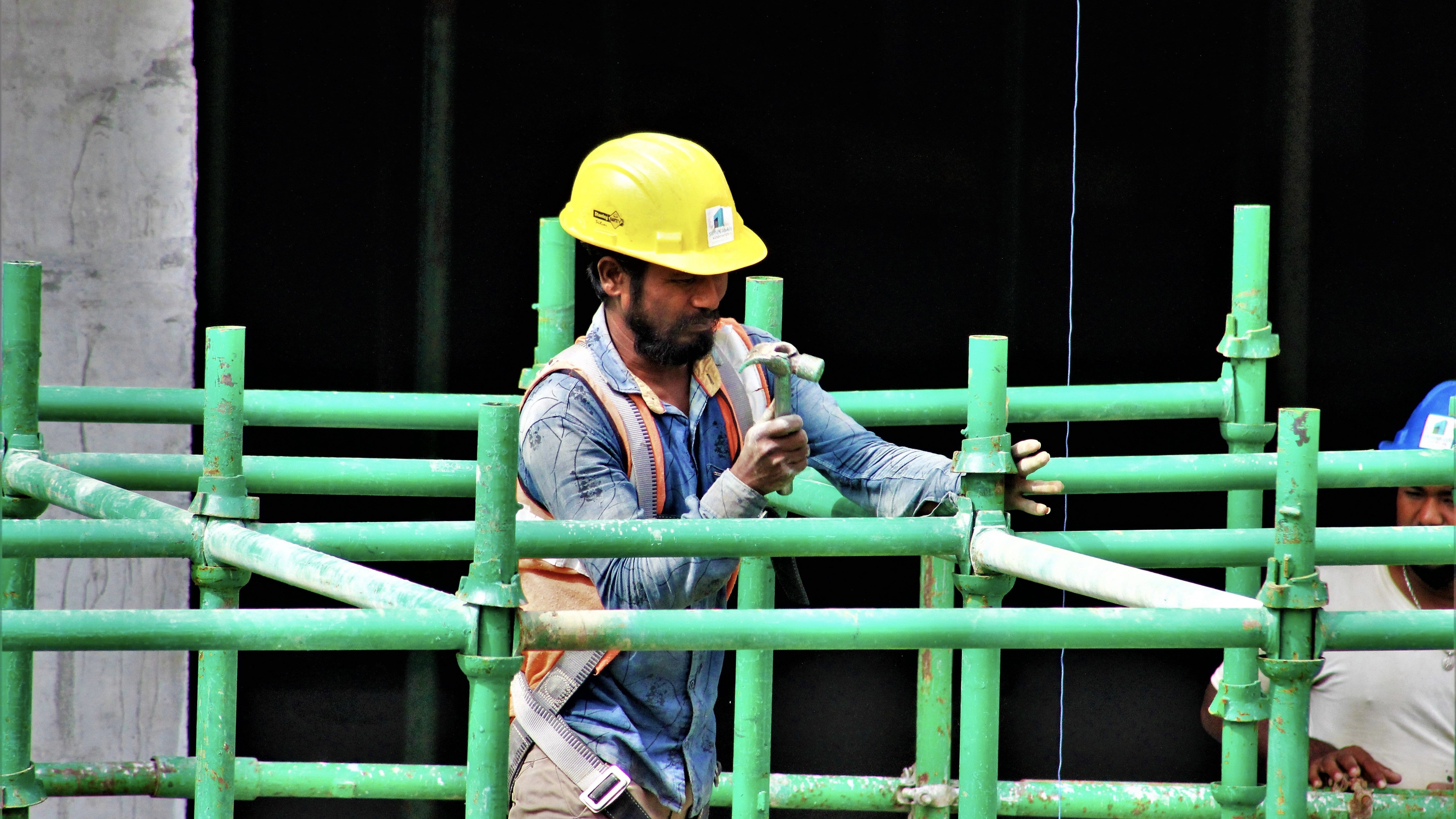 Construction worker on scaffolding at a UK building site wearing a hard hat and high visibility vest.