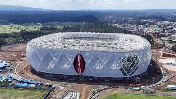 Aerial view of the Talanta Stadium construction site showing the circular steel frame and stadium bowl structure under development.