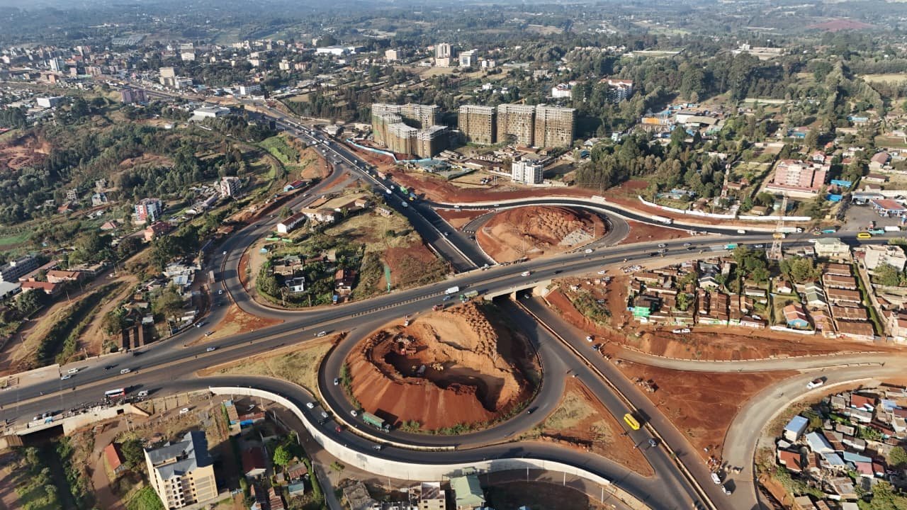 Aerial view of a complex highway interchange construction site with heavy machinery and reinforced concrete pillars in a developing urban area.
