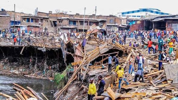 Demolished wooden structures and debris in a crowded section of Gikomba market with people standing nearby.