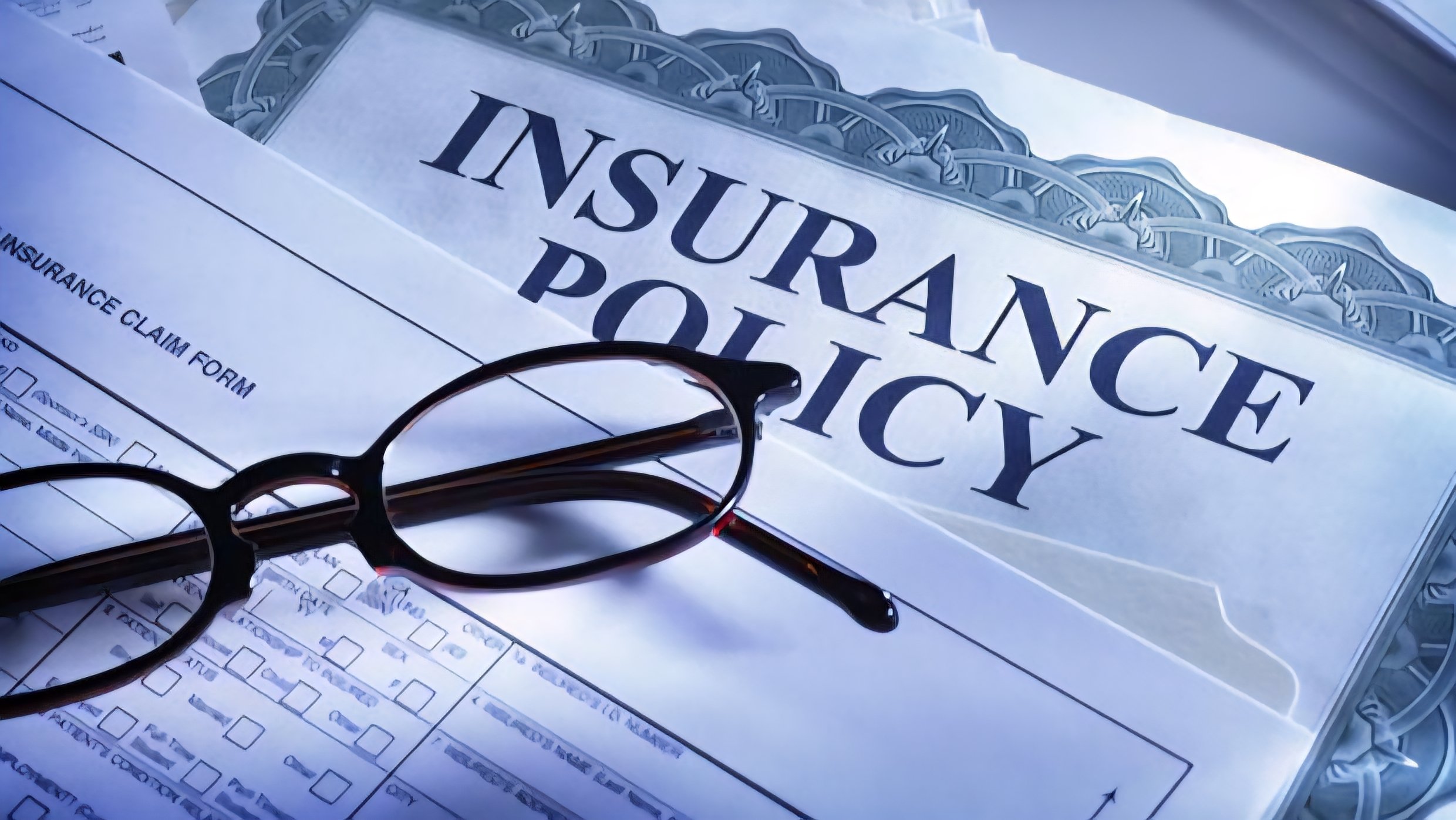 A pair of reading glasses resting on top of a formal insurance policy document and a claim form.
