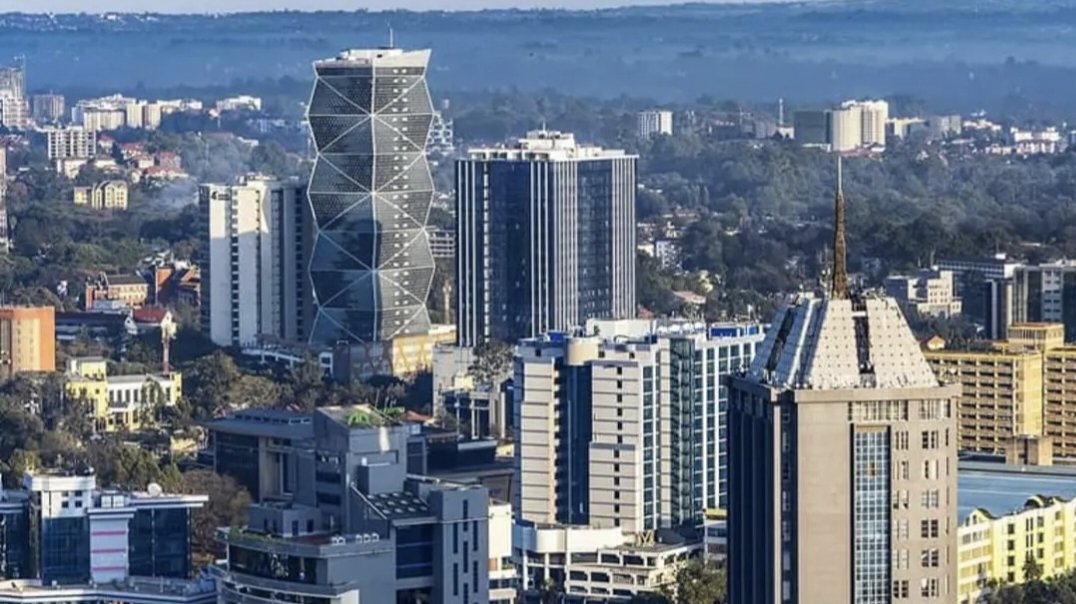 Aerial view of Nairobi's Upper Hill skyline showing multiple glass high-rise towers including the Britam Tower and UAP Old Mutual Tower rising above the city against a cloudy sky.