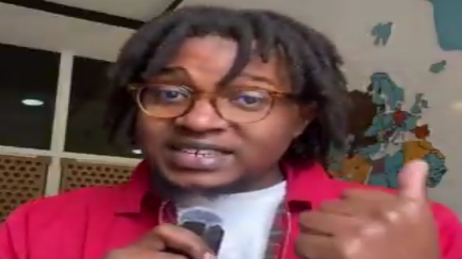 Dennis Musau, Tech Correspondent at Business Daily, speaking into a handheld microphone against an office backdrop with a world map.