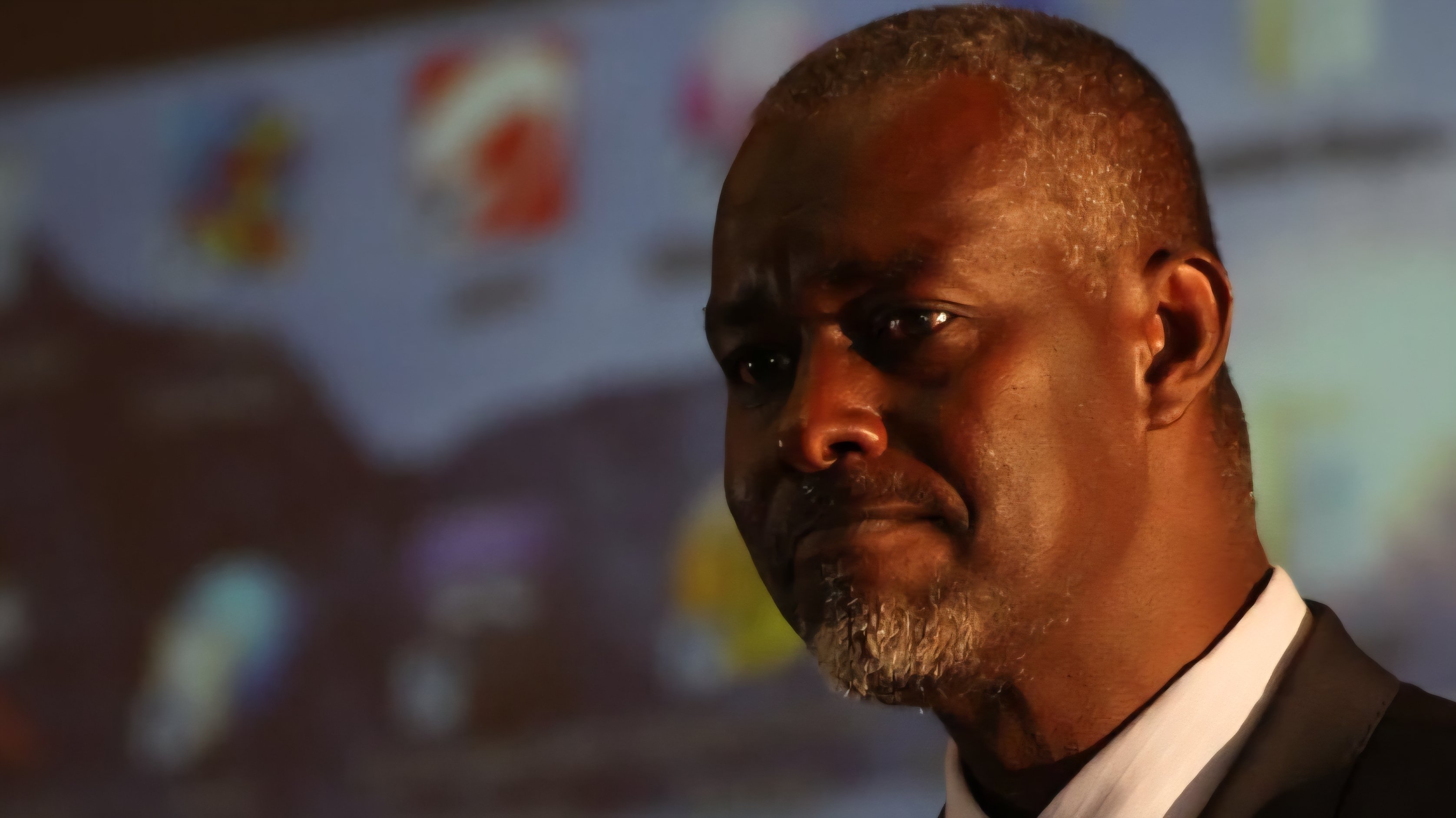 A portrait of Justice Mohamed Abdulahi Warsame, wearing a dark suit and tie, looking toward a presentation screen during a formal event.
