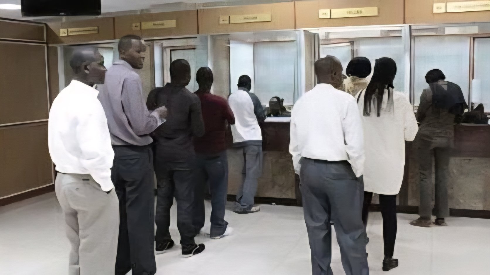 A queue of people at a bank teller window inside a Kenyan SACCO branch office.