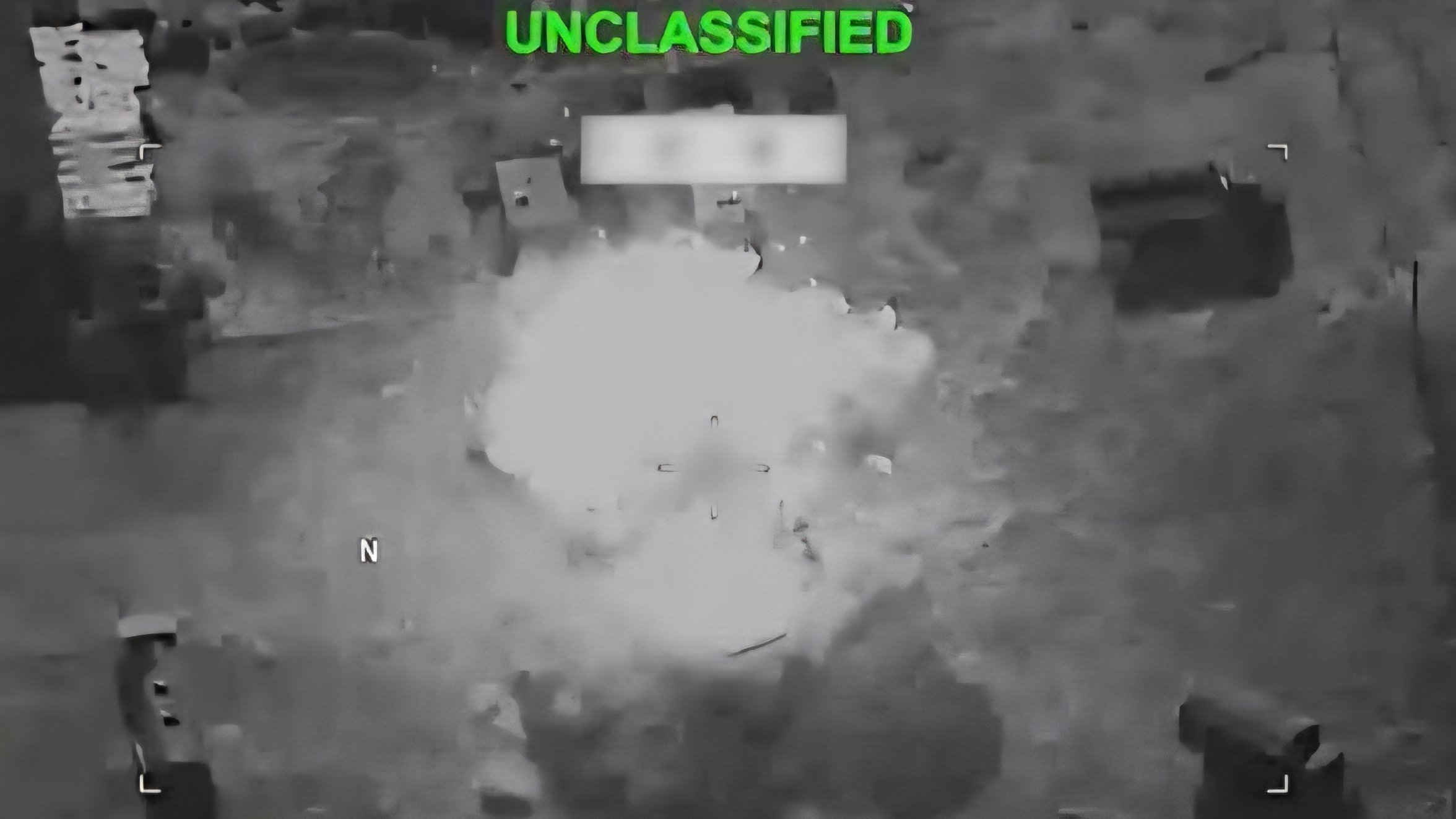 Black and white aerial reconnaissance view showing smoke rising from a military target following an airstrike in Iran.
