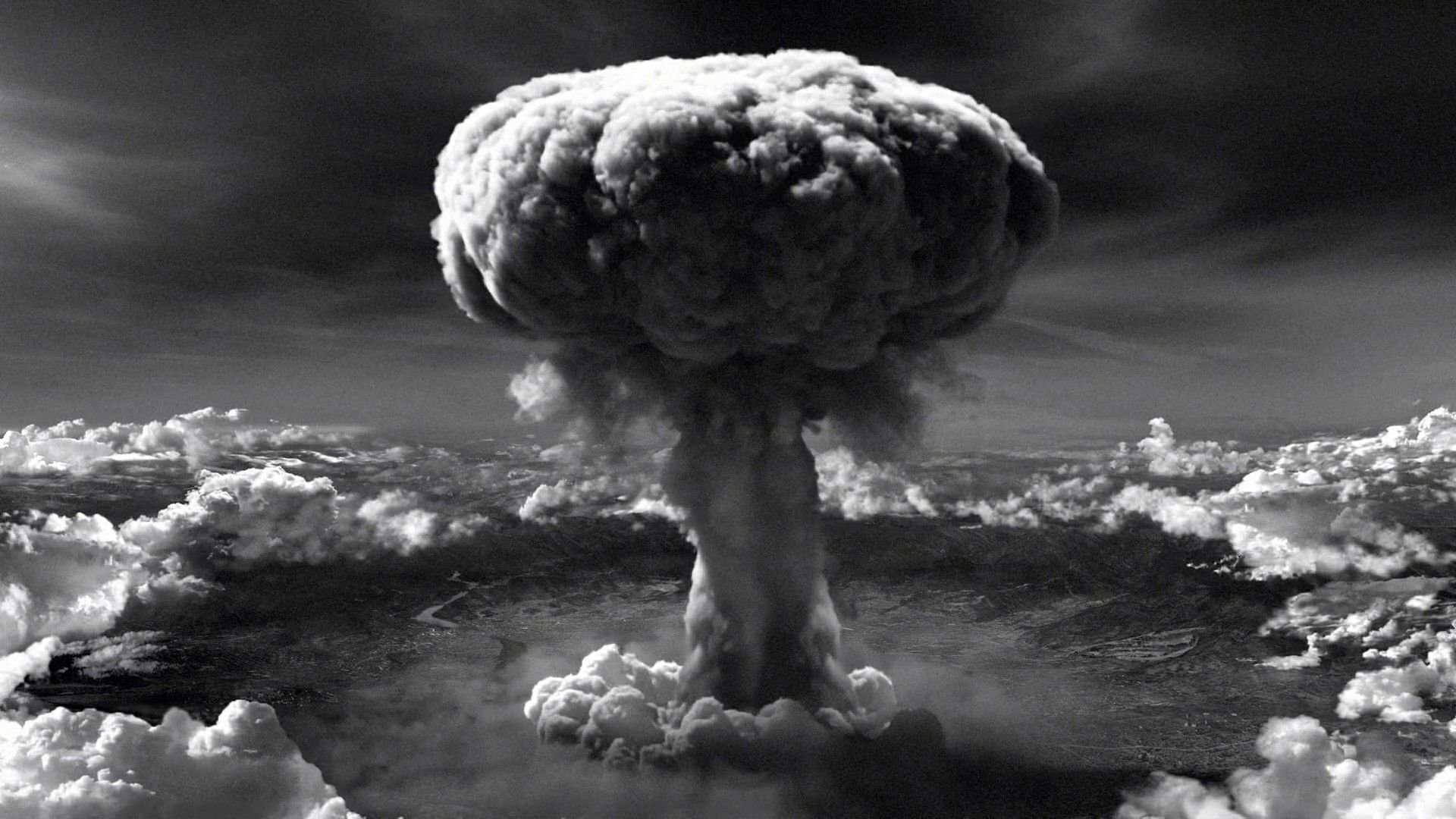 Historical black and white photograph showing a massive mushroom cloud rising over the city of Hiroshima following the atomic bomb explosion in 1945.