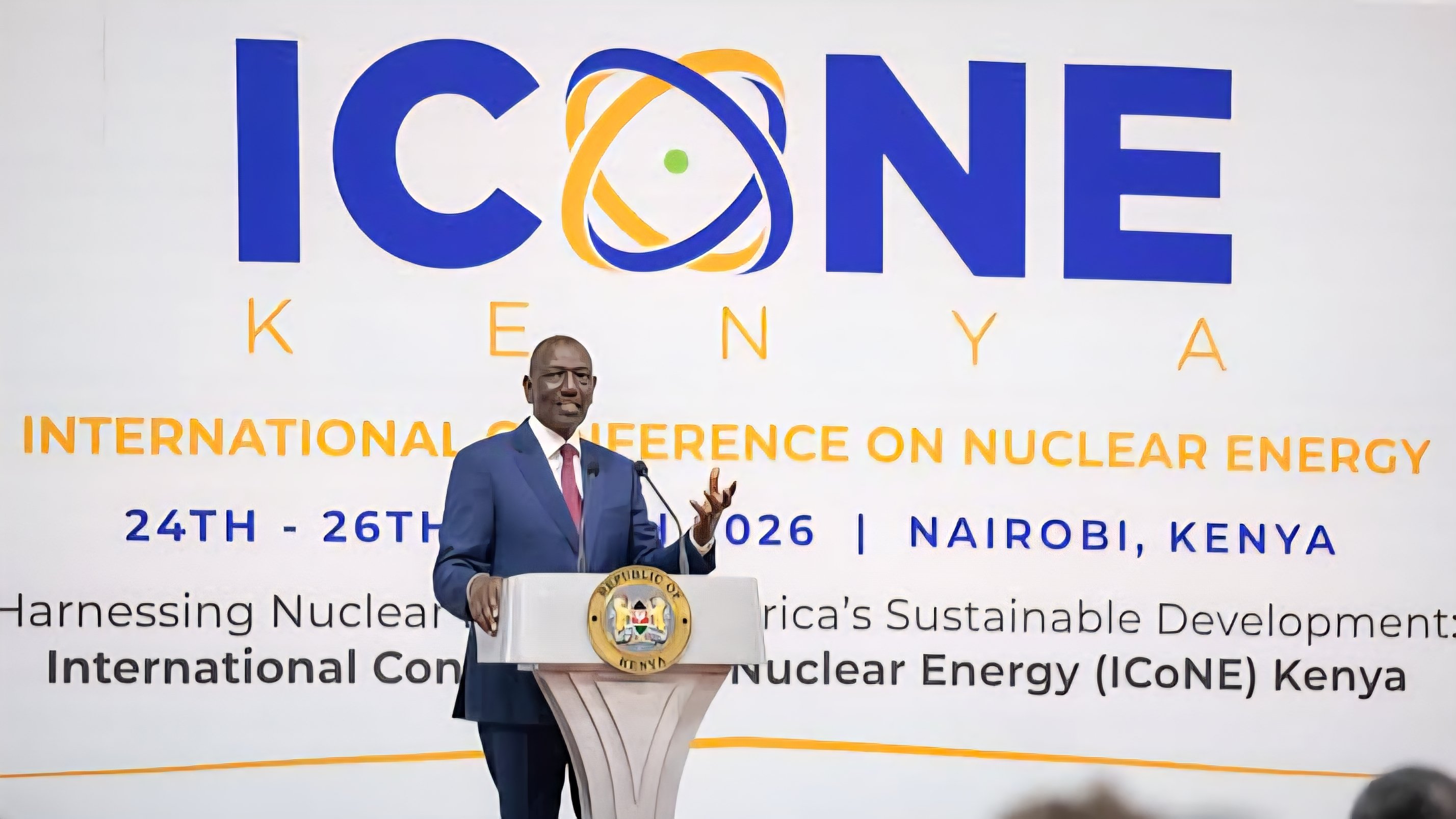 President William Ruto standing at a white podium with the Republic of Kenya seal, speaking in front of a large ICoNE Kenya International Conference on Nuclear Energy banner at the KICC in Nairobi.