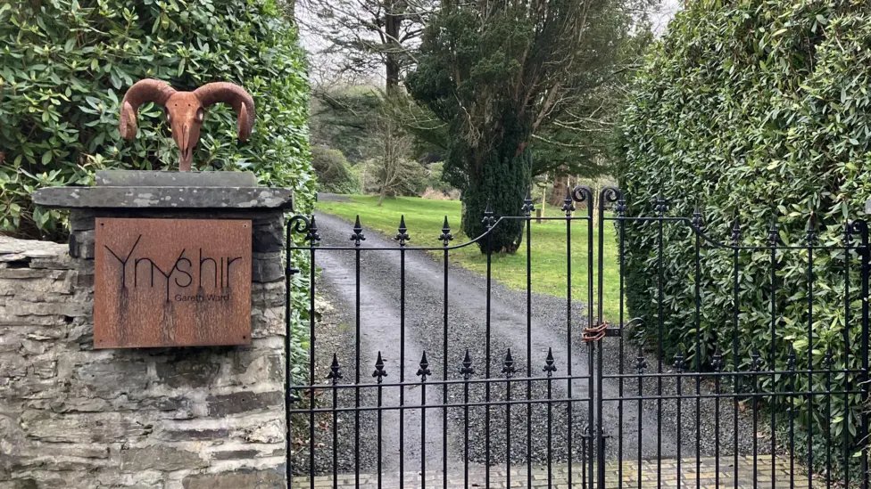 Entrance gate and stone plaque at Ynyshir restaurant in Wales surrounded by green foliage.