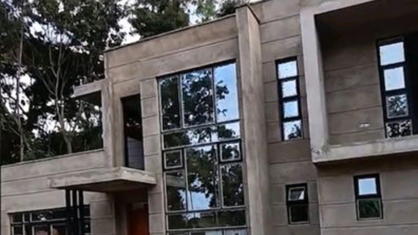 A two-story modern residential building with a raw plaster finish and large glass windows.