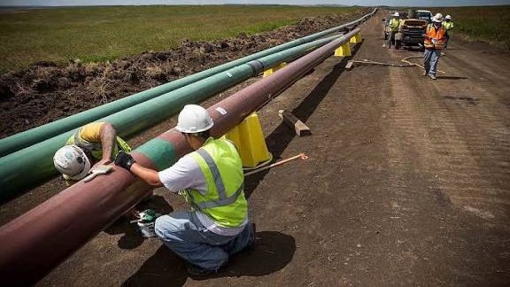 Construction workers and heavy machinery during the installation of a large diameter water transmission pipeline in a cleared corridor.