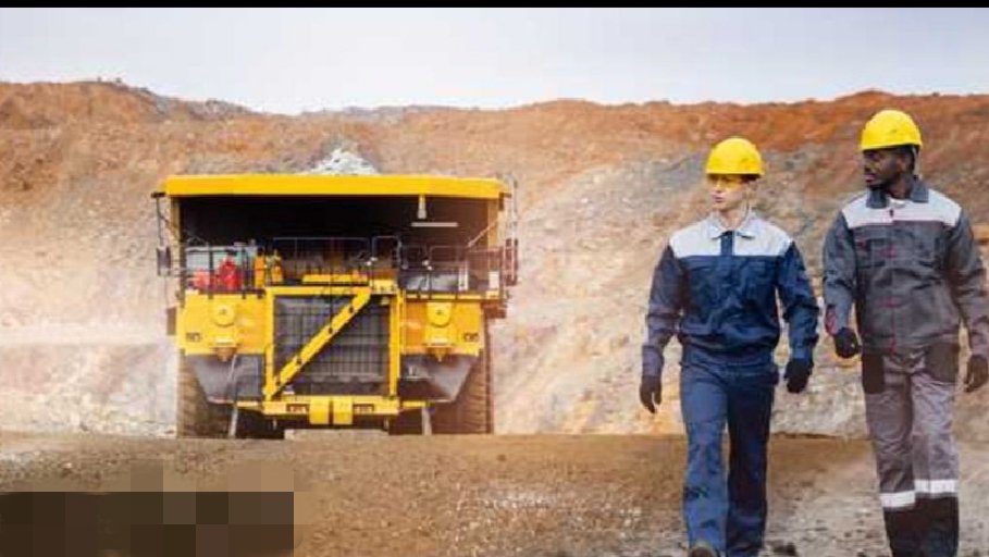 Two workers in hard hats walking past a large yellow mining truck at an open-pit mine