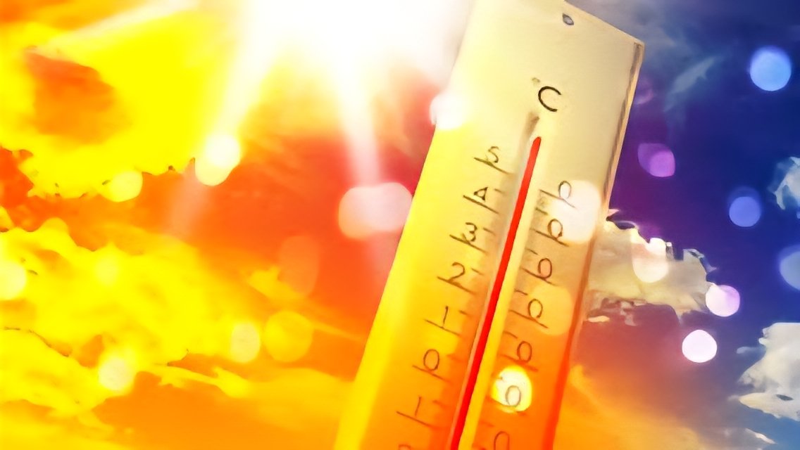 Close-up of a yellow outdoor thermometer showing high temperatures against a bright, sun-drenched sky with lens flare.