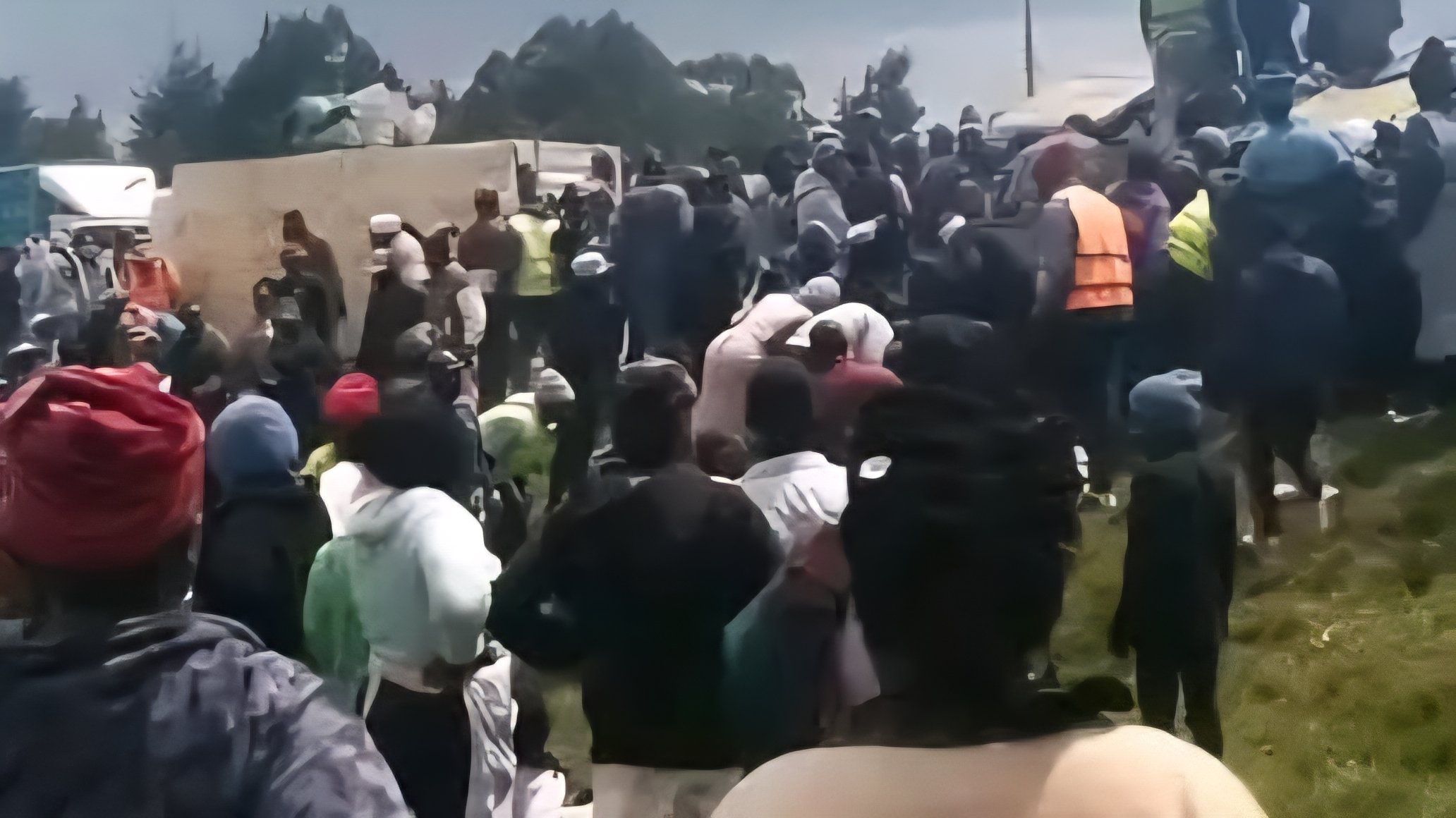 A commercial lorry and a passenger matatu lying on their sides on a paved highway near a flyover structure with onlookers and emergency responders nearby.