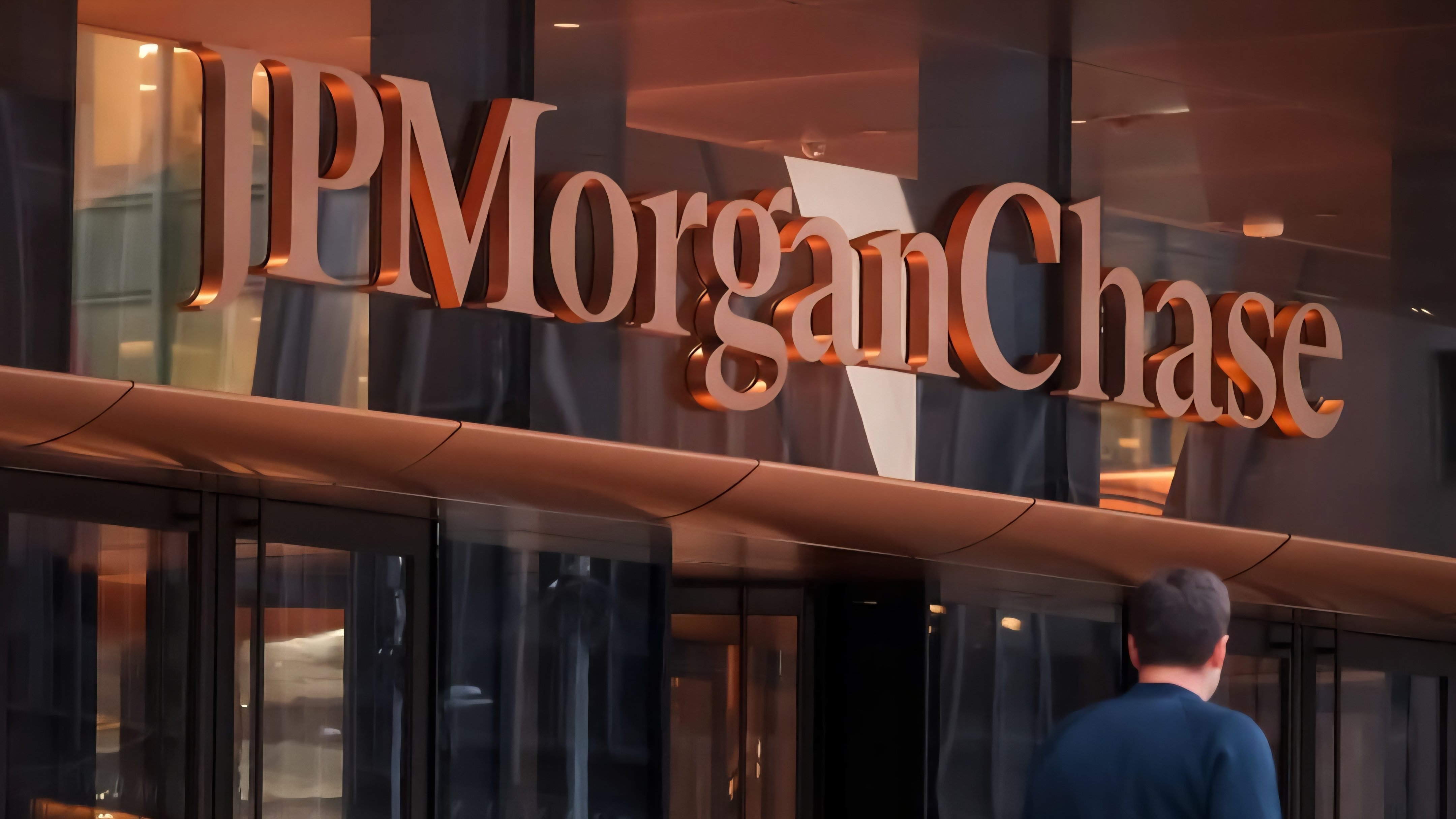 A view of the JPMorgan Chase office entrance with employees walking outside the glass doors under the company logo.