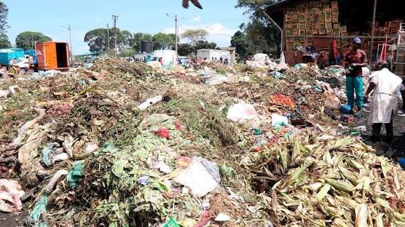 Large piles of organic market waste and discarded agricultural by-products accumulated at an open-air collection point in a busy urban area.