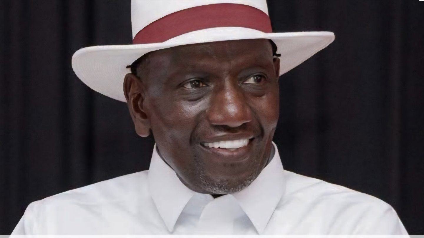 A close-up graphic of President William Ruto wearing a white shirt and a matching wide-brimmed hat, overlaid with a quote about the completion of 28 new stadiums in Kenya.
