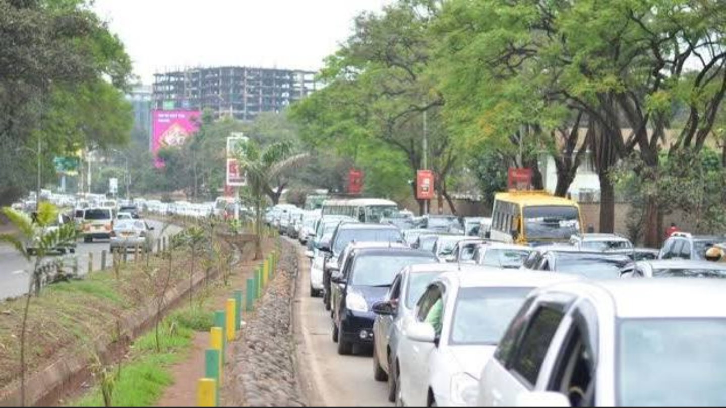 Traffic congestion along Uhuru Highway in Nairobi with vehicles lined up in multiple lanes amid trees and roadside greenery.