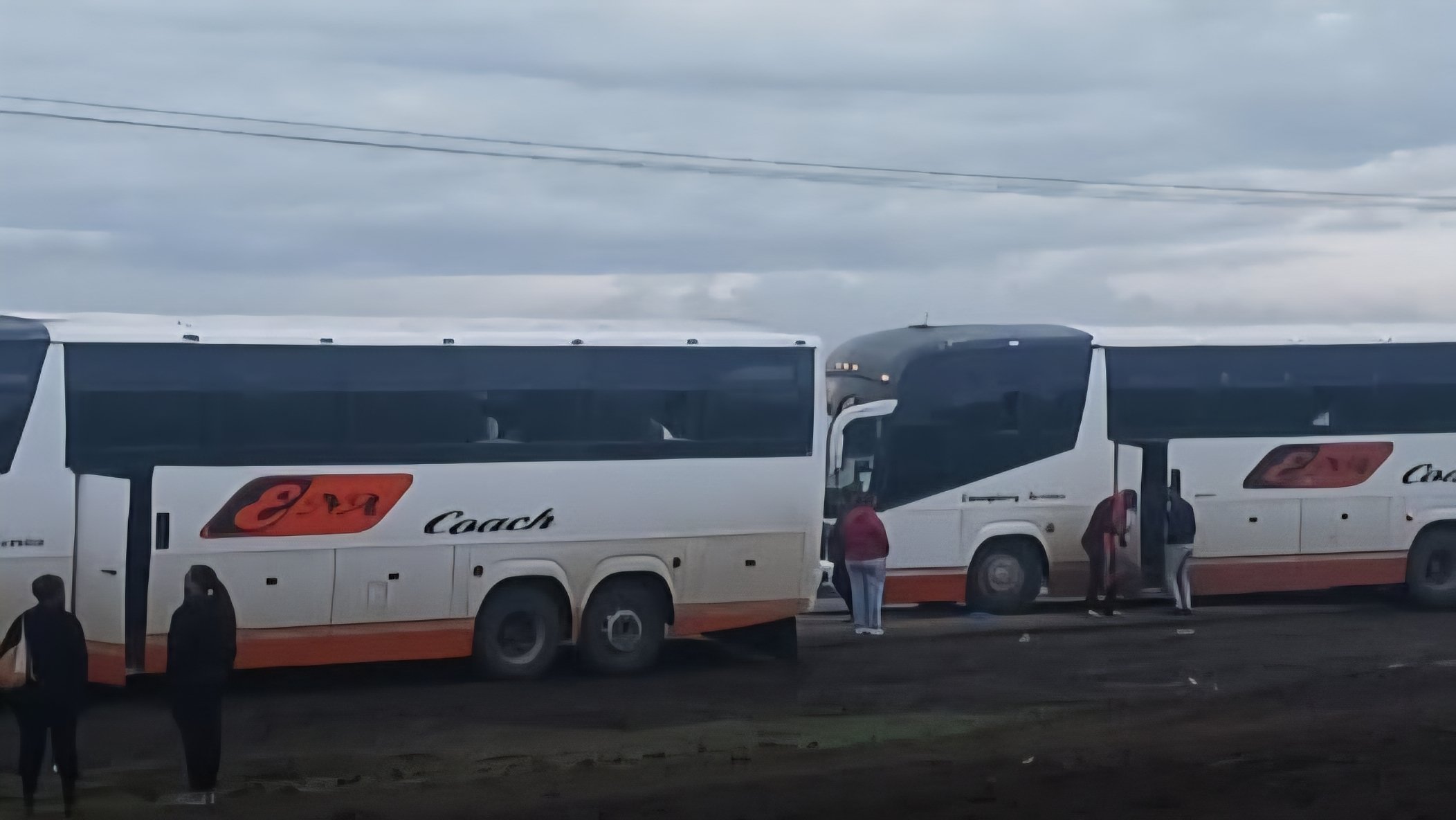 Two Ena Coach buses parked at a terminal on a cloudy day with passengers boarding.