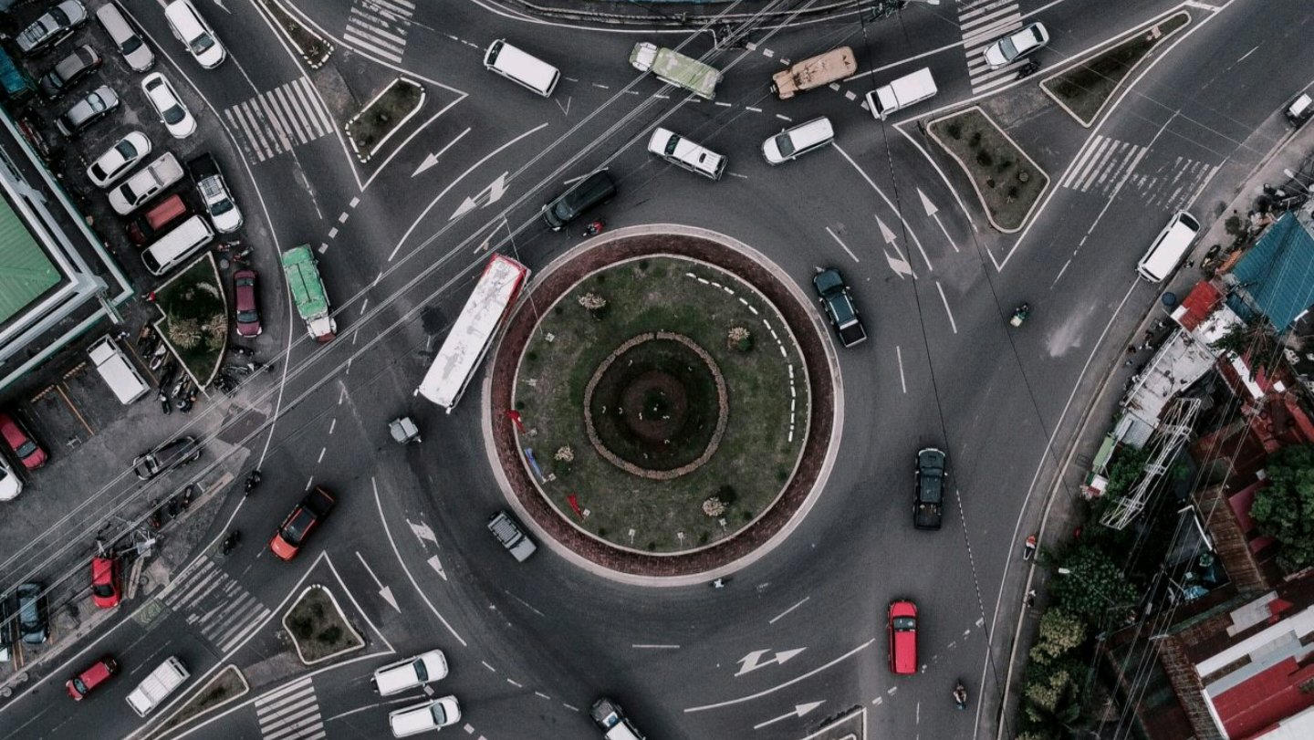 Aerial view of a multi-lane urban roundabout with circulating traffic, central landscaping, and connecting roads.