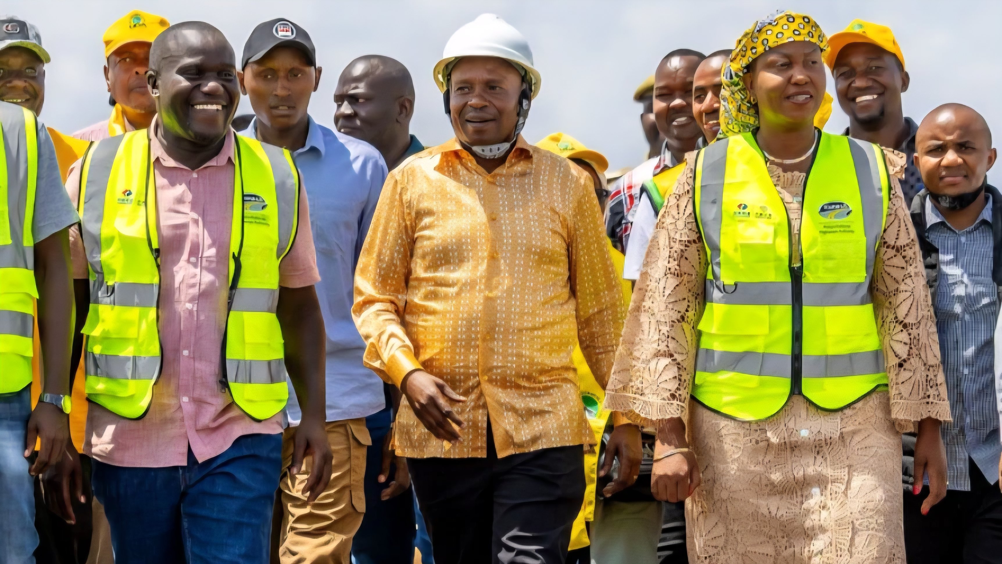 Deputy President Kithure Kindiki wearing a yellow shirt and white hard hat walking with officials at a road construction site in Kenya.