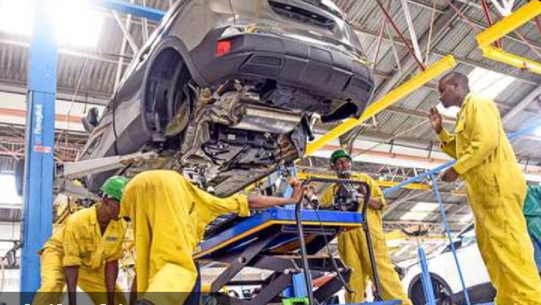 Technicians in yellow overalls working on a vehicle chassis inside a professional automotive assembly plant in Kenya.