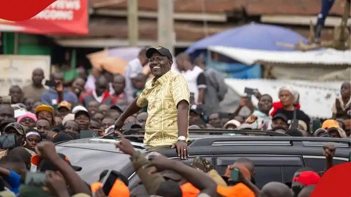 President Ruto waving to a large crowd from an open-roof vehicle during a public event in Kenya.