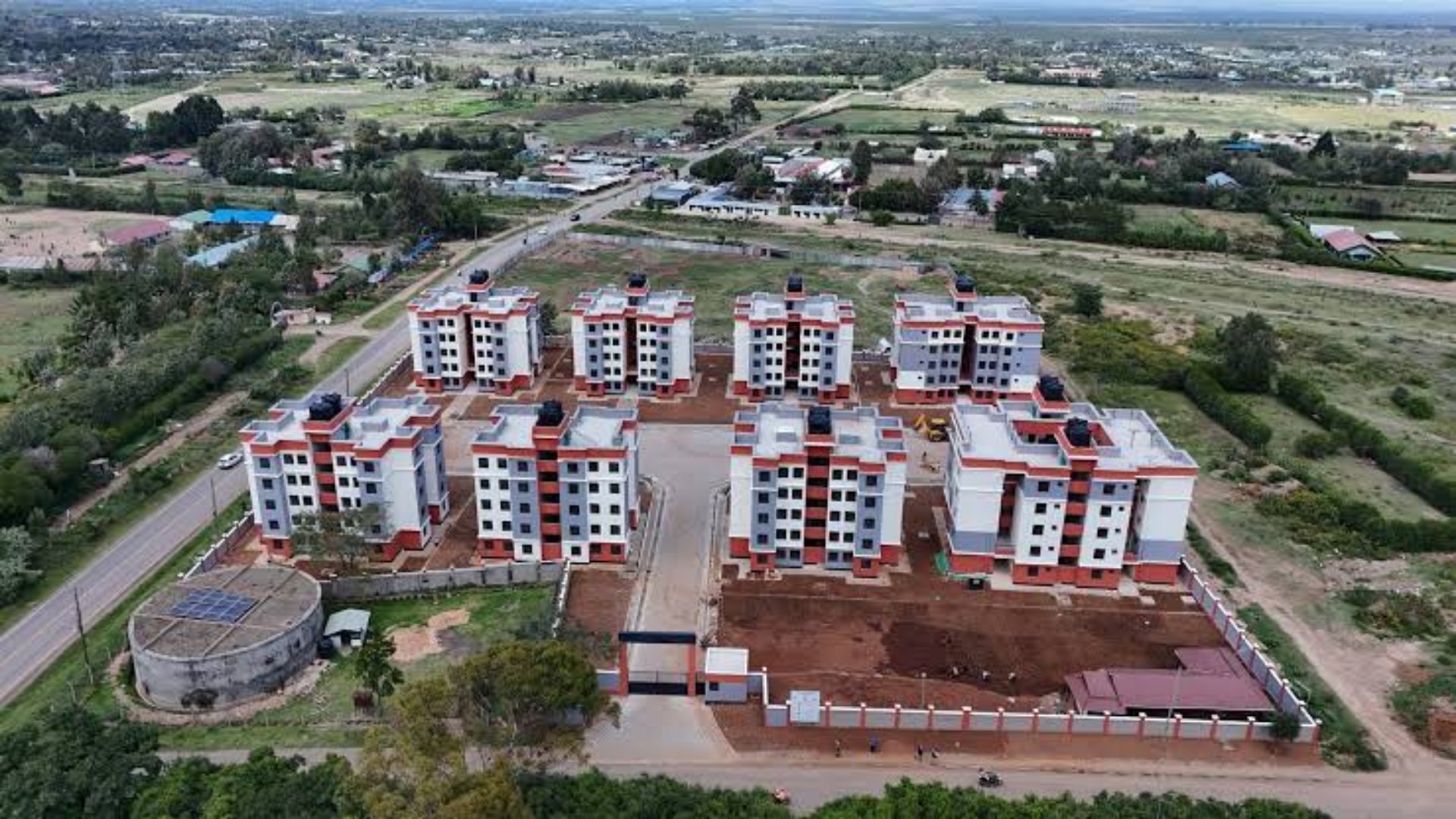 A construction site in Kenya showing a completed high-rise affordable housing block next to a newly commenced commercial strip mall foundation.