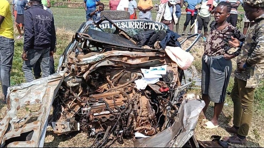 A severely damaged vehicle wreckage sitting in a field in Kirinyaga County following a fatal head-on collision along the highway.