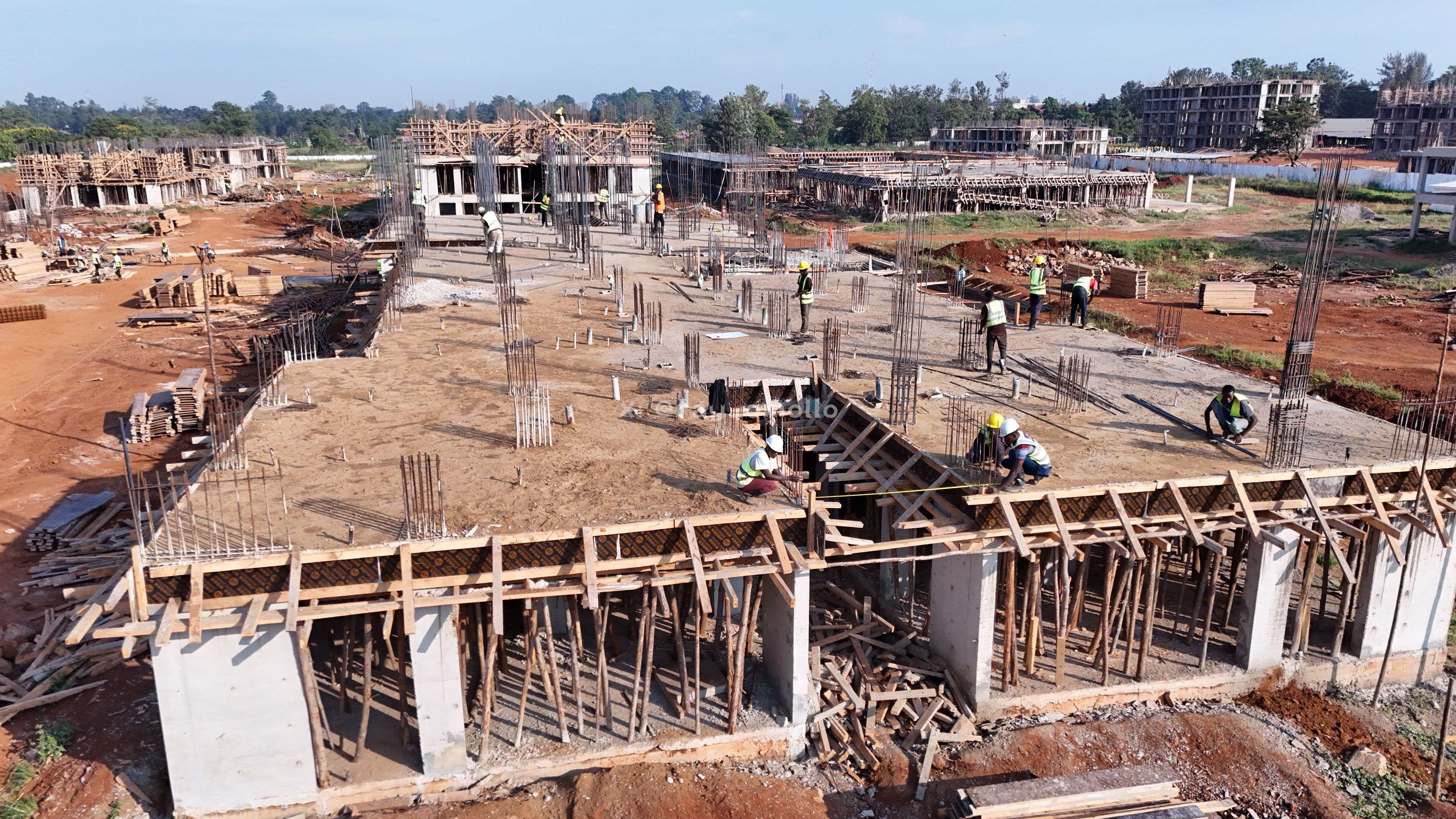 High-angle view of an active construction site in Busia showing concrete slabs, timber scaffolding, formwork, and construction workers installing reinforcement bars.