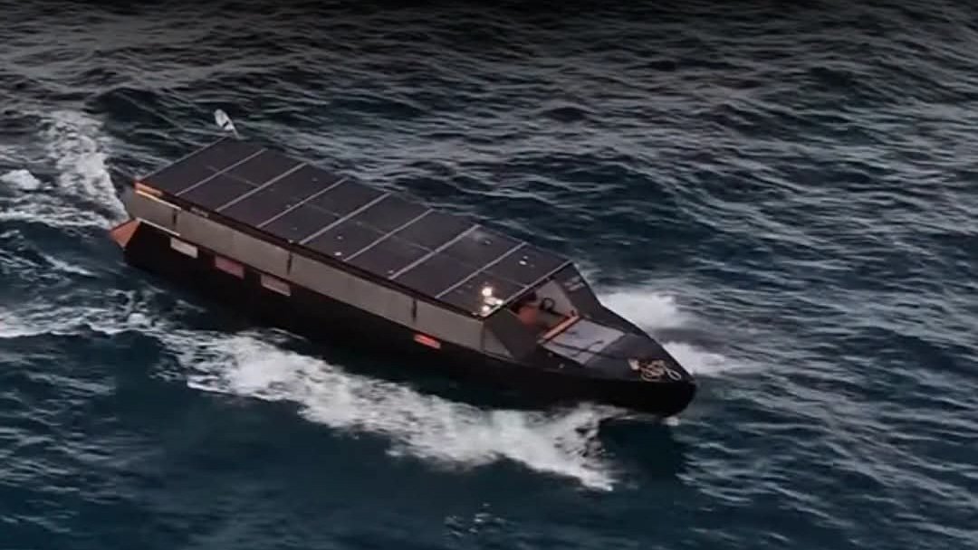 An 11-meter solar-powered yacht named Helios 11 navigating open ocean water under clear blue skies.
