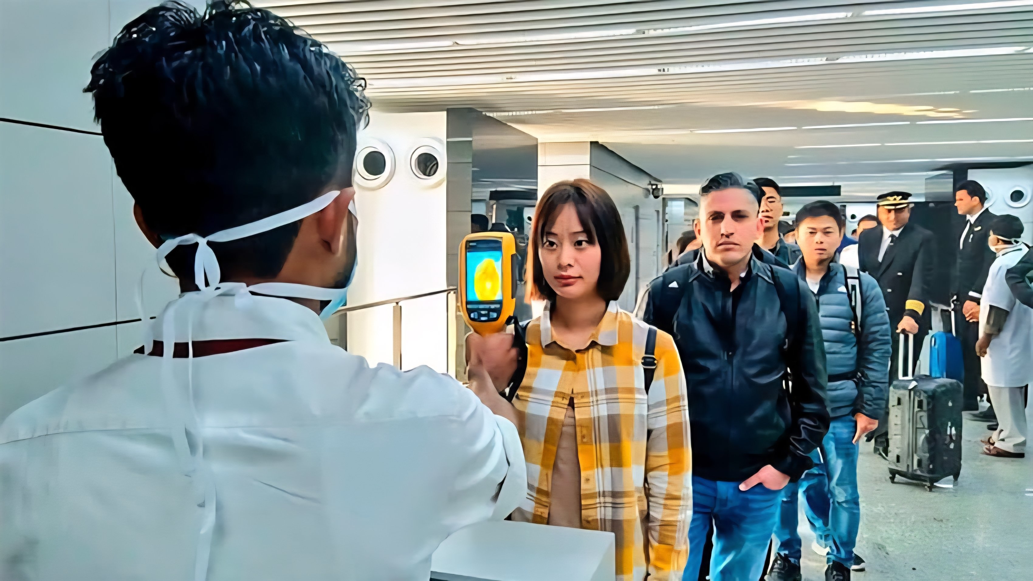 Health official wearing reflective vests and masks conduct health screenings and temperature checks for passengers arriving at an international airport terminal.