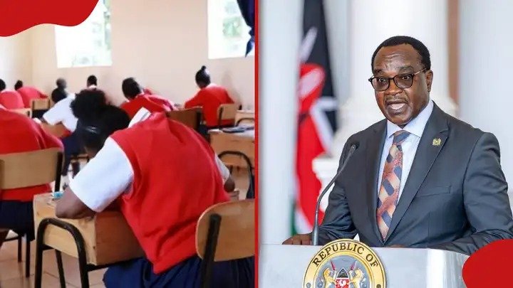 A student in a red sweater sits at a wooden desk in a classroom while Education Cabinet Secretary Julius Ogamba speaks from a podium.