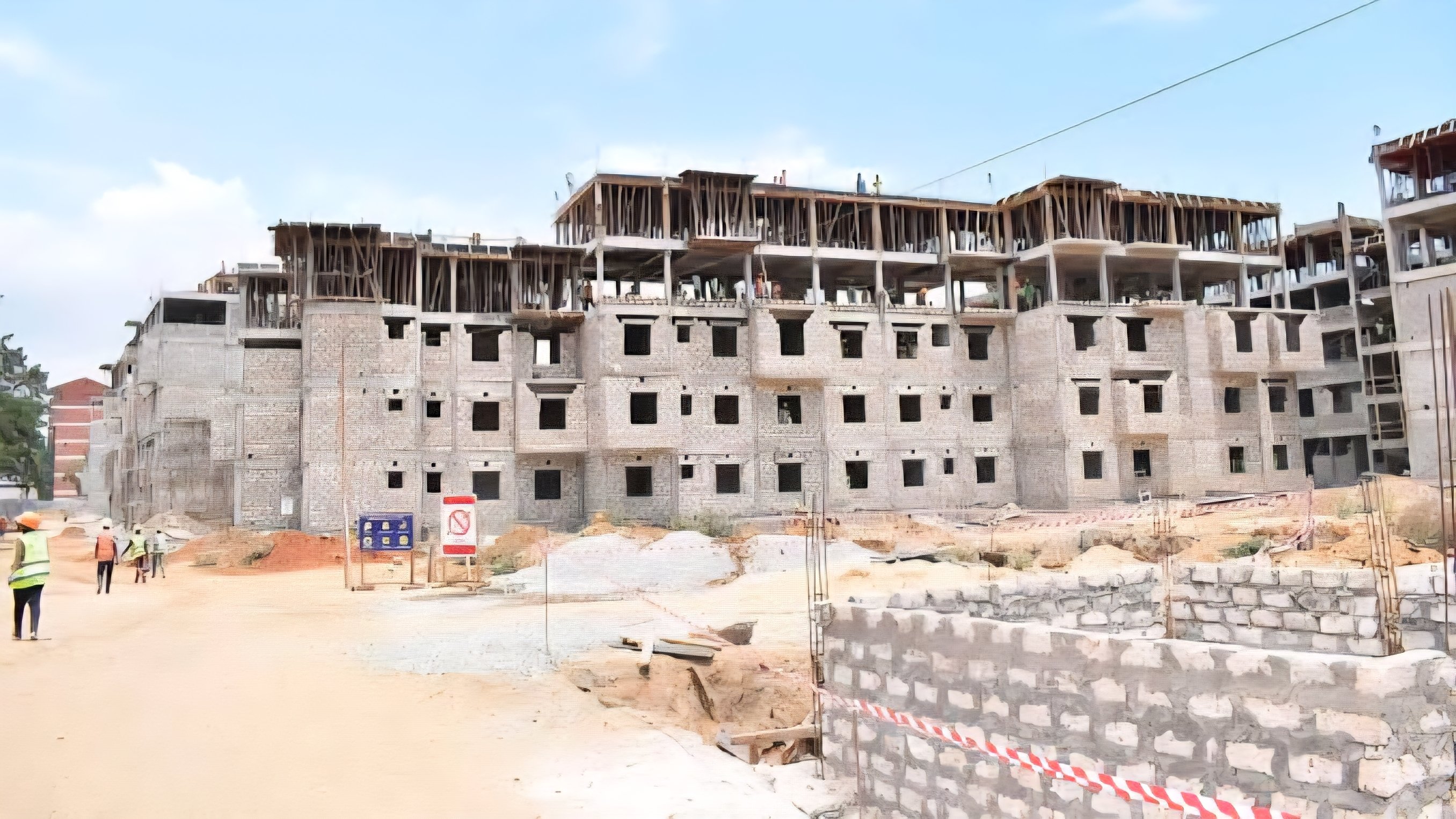 A high-angle view of a multi-story apartment block under construction with scaffolding and laborers visible on the upper floors.