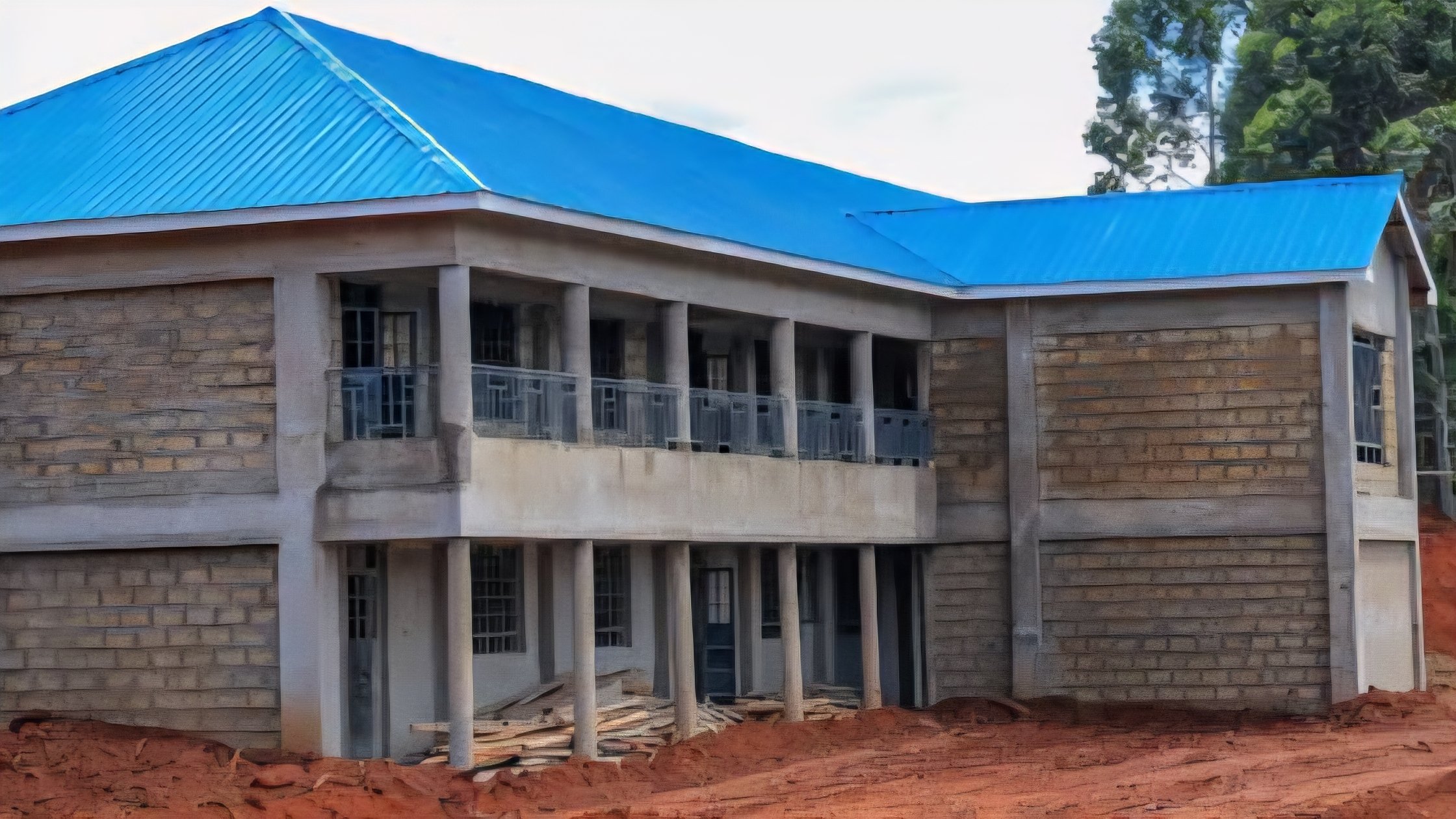 A row of unfinished stone classrooms with open window frames and no roof at a public secondary school in Kenya