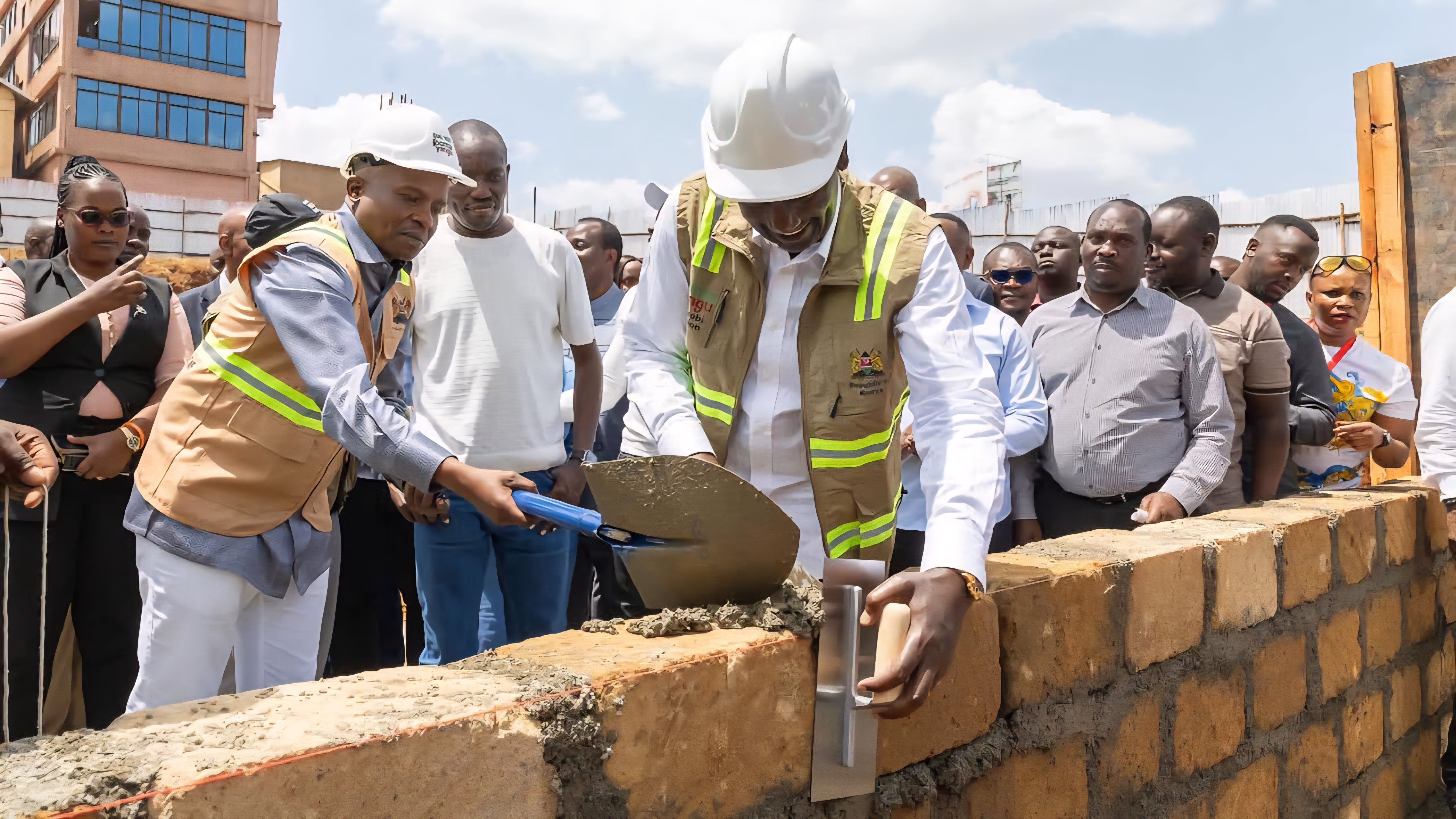 A close-up view of a ceremonial foundation stone laid in a bed of wet mortar and surrounded by concrete blocks at a construction site in Kisii.