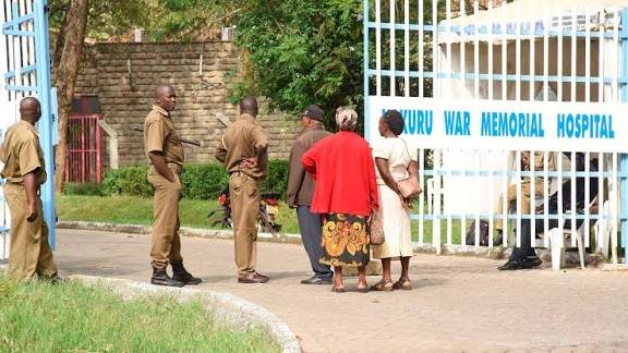 Armed police officers and civilians standing at the gated entrance of Nakuru War Memorial Hospital.