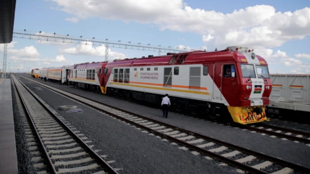 Passenger train arriving at Nairobi railway station on elevated tracks with urban skyline in background.