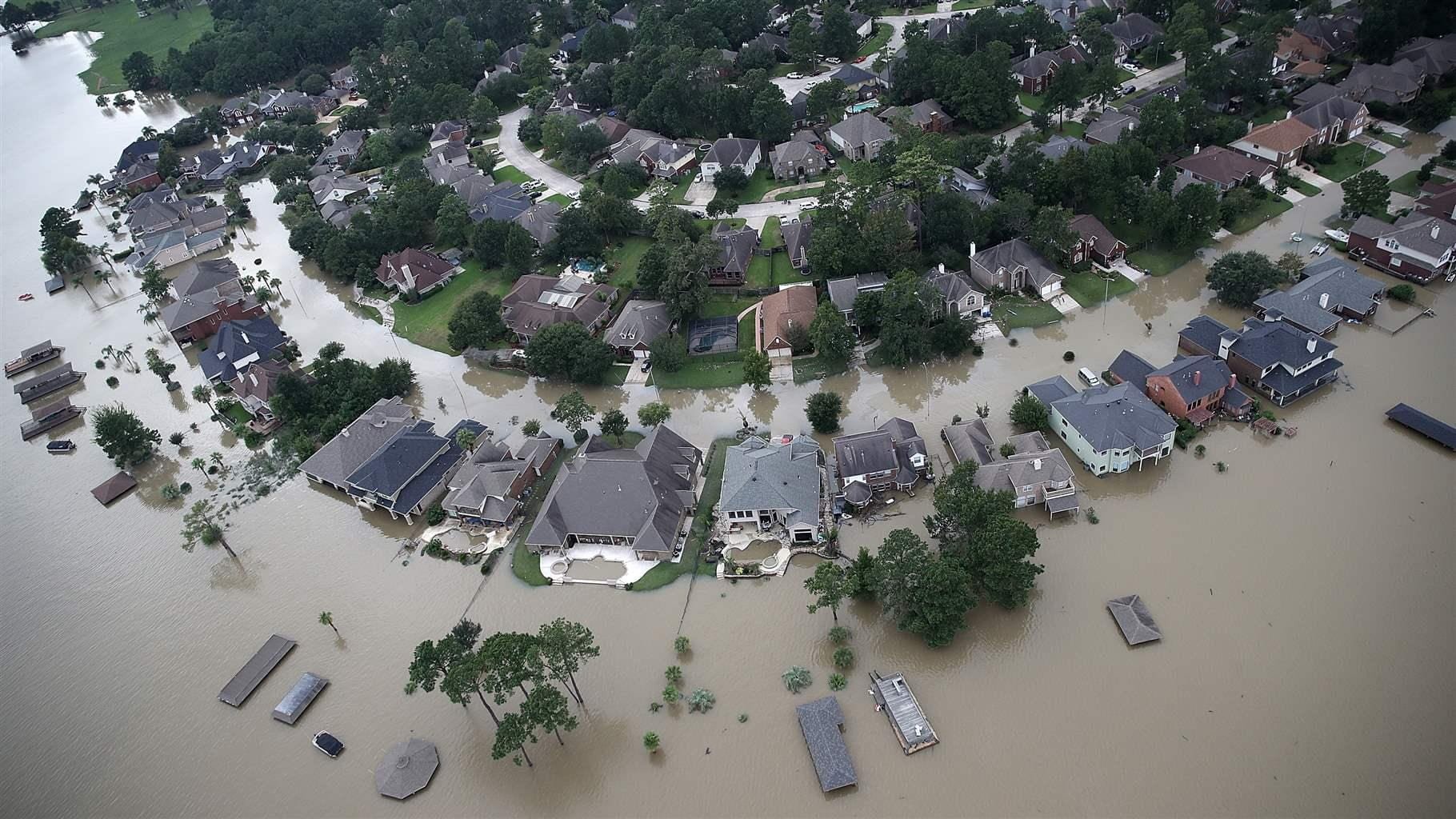 Aerial view of a flooded urban neighbourhood with submerged streets and partially inundated buildings, illustrating the impact of extreme weather events on built environments.